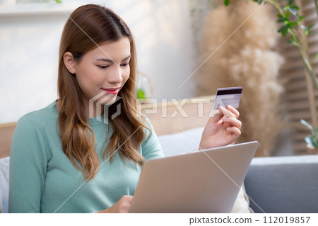 Young asian woman sitting on sofa using laptop computer shopping online with credit card. 112019857