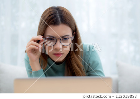 Concentrated young asian woman wearing glasses working on laptop with commitment. Concentrated young asian woman wearing glasses working on laptop with commitment. 112019858