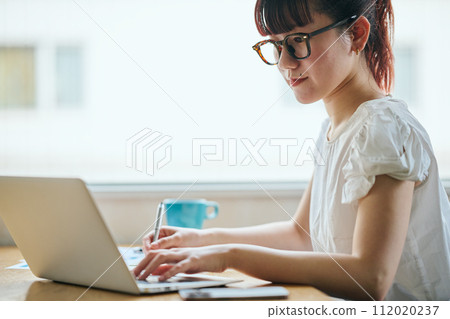 Young woman jotting down notes while operating a computer 112020237