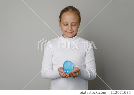 Young kid girl holds in her hands silicone trainer for alignment of the teeth  112021683