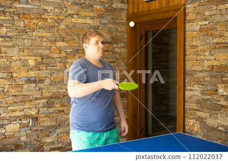 Young man playing ping pong. He holds a racket in his hands. Table tennis. The concept of sport and healthy lifestyle. Young man playing ping pong. He holds a racket in his hands. Table tennis. The concept of sport and healthy lifestyle. 112022037