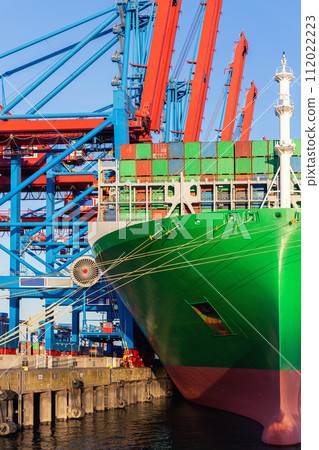Scenic view giant cargo container ship loading Hamburg city port harbor against seaport cranes warm evening sunset lights. Global commercial trade freight charter shipping and logistics background 112022223