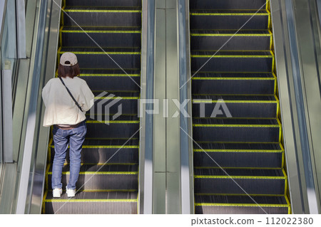 A young woman riding an escalator in an office building in front of Nagoya station 112022380