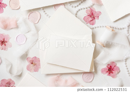 Card and envelope near pink decorations, seals and silk ribbons on white table top view, wedding mockup Card and envelope near pink decorations, seals and silk ribbons on white table top view, wedding mockup 112022531