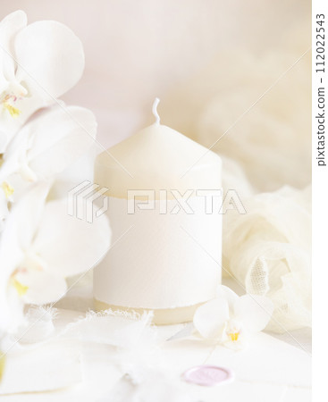 Pillar candle with a blank label near white orchid flowers close up, pastel romantic mockup Pillar candle with a blank label near white orchid flowers close up, pastel romantic mockup 112022543