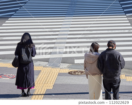 A business woman and a young couple are waiting at a traffic light at a crosswalk at a city intersection on a winter day. 112022629