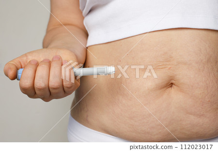 Female belly and hand closeup with Semaglutide Injection pen or insulin cartridge pen. Female belly and hand closeup with Semaglutide Injection pen or insulin cartridge pen. 112023017