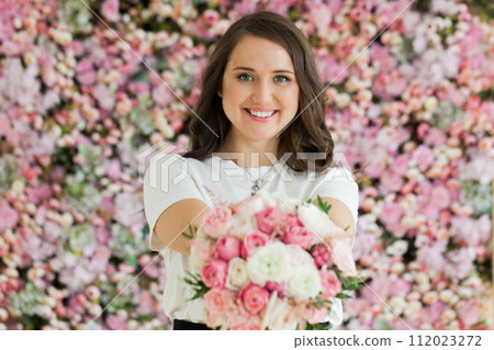 Happy female model taking rose flower standing on blooming floral blossom background.  112023272