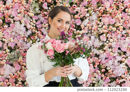 Perfect female model with rose flower in her hand standing on blooming floral blossom background. Perfect female model with rose flower in her hand standing on blooming floral blossom background. 112023280