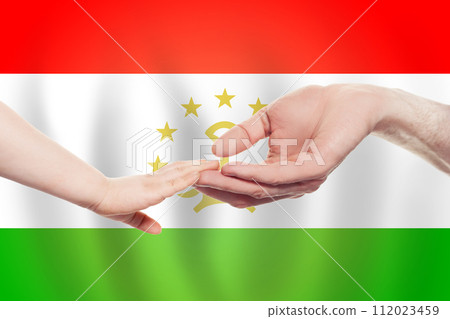 Tajikistani baby and parent hands on the background of flag of Tajikistan Help Tajikistani baby and parent hands on the background of flag of Tajikistan Help 112023459