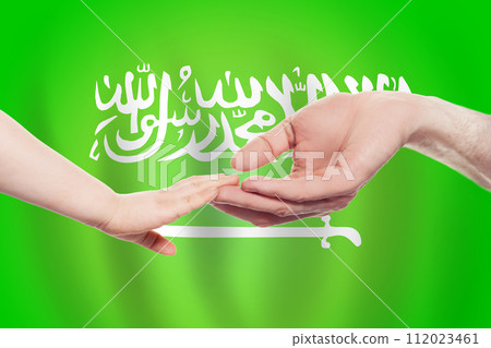 Saudi Arabian baby and parent hands on the background of flag of Saudi Arabia Help 112023461