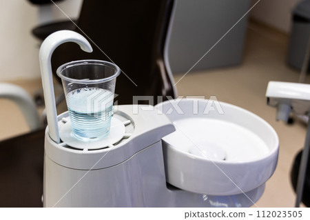 Disposable glass filled with CHX mouth rinse next to spiotoon bowl in dental clinic Disposable glass filled with CHX mouth rinse next to spiotoon bowl in dental clinic 112023505