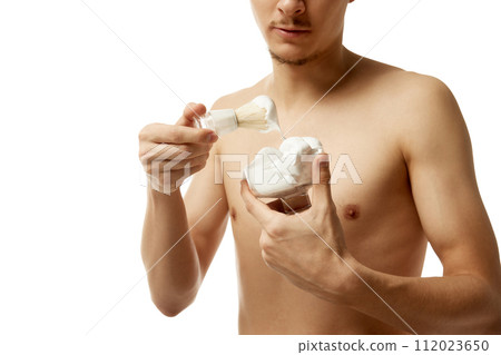 Cropped portrait of man holds container of shaving foam and shaving brush looking at camera against white studio background. Cropped portrait of man holds container of shaving foam and shaving brush looking at camera against white studio background. 112023650