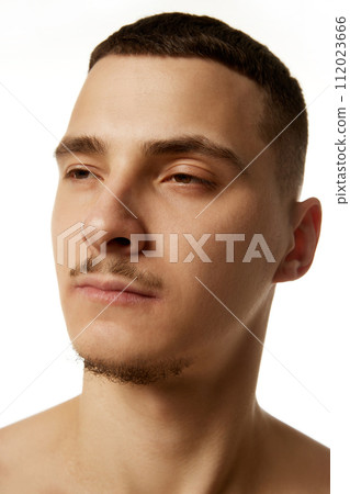 Close-up side view of shirtless man with a trimmed beard, looking away with neutral expression against white studio background. Close-up side view of shirtless man with a trimmed beard, looking away with neutral expression against white studio background. 112023666