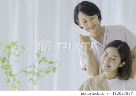 一位臉上疼痛的年輕女子正在接受中年女性脊椎按摩師的按摩 112023857