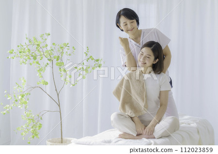 一位臉上疼痛的年輕女子正在接受中年女性脊椎按摩師的按摩 112023859