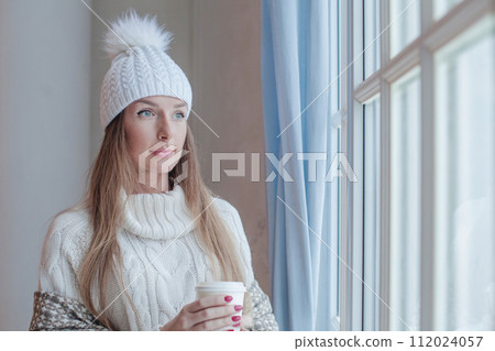 Cheerful winter woman holding hot dring and resting at home, romantic portrait 112024057