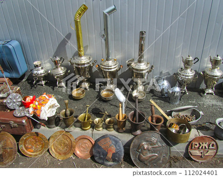 Swap meet. Ancient objects - samovars, mortars, copper plates lie on the ground. Flea market, second hand, used items 112024401