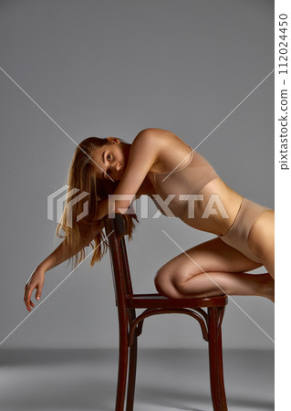 Sensual, tender, young woman with slim, fit body posing on chair in underwear against gray studio background Sensual, tender, young woman with slim, fit body posing on chair in underwear against gray studio background 112024450