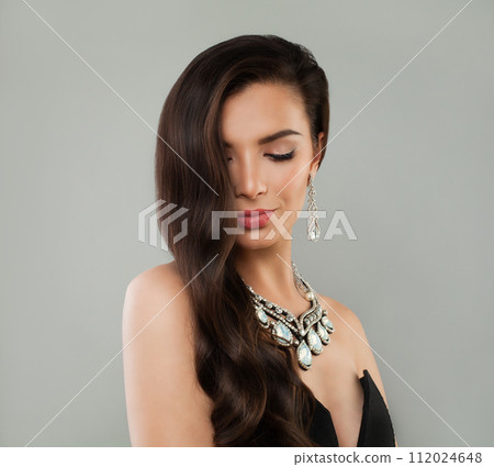 Elegant brunette model woman with long wavy hairdo, diamond jewelry earring and necklace  112024648