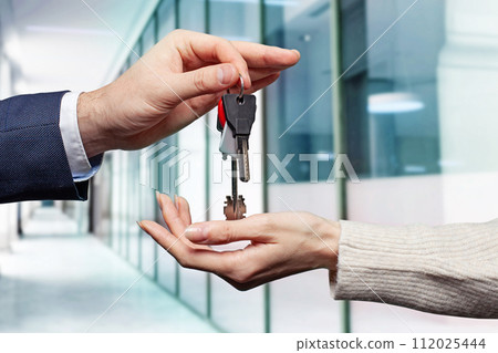 Real estate concept. Estate agent giving house keys against abstract modern office  112025444