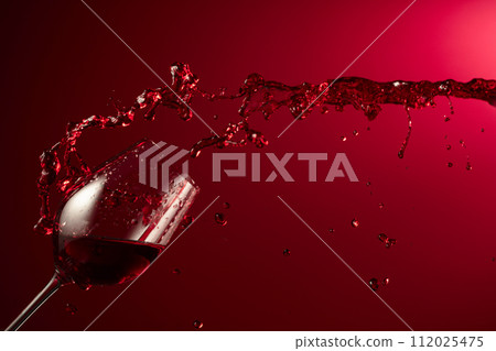 Glass and red wine splash on a dark red background. 112025475