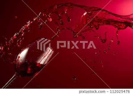 Glass and red wine splash on a dark red background. 112025476