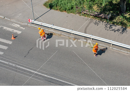 Municipal cleaners manually sweep the city roadway Municipal cleaners manually sweep the city roadway 112025584