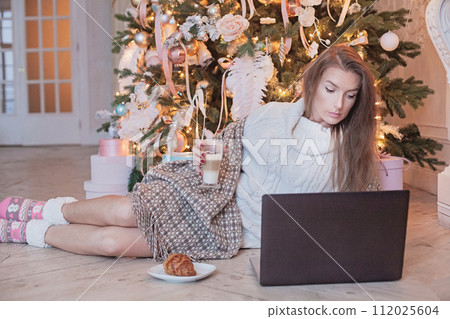 Winter portrait of pretty brunette woman using laptop drinking coffee sitting on vintage floor 112025604