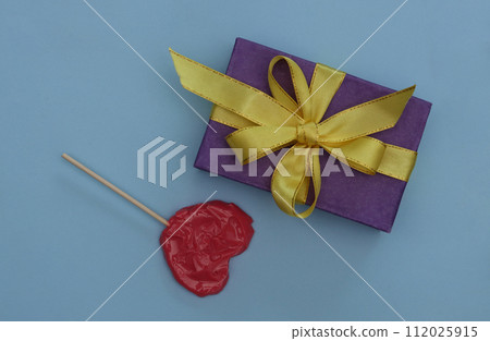 Gift box and heart shaped lollipop on a blue background. 112025915