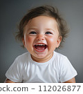 Excited baby boy on a gray background smiling and looking at the camera. Studio shot of an amused small baby with short hair. Cute cheerful child with an open mouth and small white teeth. 112026877