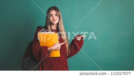 Happy female university student pointing to copy space and holding books 112027077