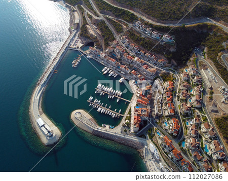 Aerial view of Lustica Bay, Adriatic sea, Montenegro. Top view of buildings, Harbor Marina with moored boats and yachts and lighthouse against the backdrop of mountains. New modern luxury resort Aerial view of Lustica Bay, Adriatic sea, Montenegro. Top view of buildings, Harbor Marina with moored boats and yachts and lighthouse against the backdrop of mountains. New modern luxury resort 112027086