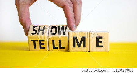 Tell or show me symbol. Businessman turns beautiful wooden cubes and changes words Tell me to Show me. Beautiful yellow table white background. Business tell or show me concept. Copy space. 112027095