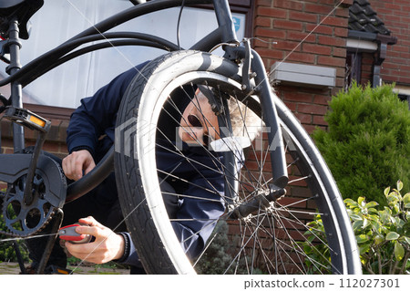 Young man in casual clothes cleaning rust and oiling his city cruiser bicycle chain and gear with spray before riding. Male doing DIY maintenance of his bicycle at home. Selective focus. Young man in casual clothes cleaning rust and oiling his city cruiser bicycle chain and gear with spray before riding. Male doing DIY maintenance of his bicycle at home. Selective focus. 112027301