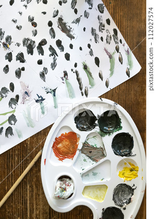 A dirty palette for mixing watercolours. On the table - a painted sheet of paper and a brush. The concept of art and hobbies for children. 112027574