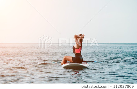 Sea woman sup. Silhouette of happy young woman in pink bikini, surfing on SUP board, confident paddling through water surface. Idyllic sunset. Active lifestyle at sea or river. 112027809