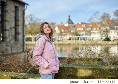 Young beautiful pretty tourist girl in warm hat and coat with backpack walking at cold autumn in Europe city enjoying her travel in Bietigheim-Bissingen, Deutschland. Outdoor portrait of young tourist 112028412