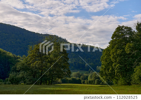 Mountain Landscape At Sunset. Scenery With Stones On The Hillside. Distant Valley Between Forested Hills In Evening Light. Picturesque Landscape Of The Mountains. Mountainous Landscape At Sunset 112028525