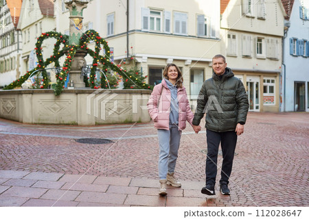 Loving couple of tourists walking around old town. Couple of lovers leisurely stroll in the cool autumn morning on the streets of a BIETIGHEIM-BISSINGEN (Germany). The guy holds his wife. Vacation Loving couple of tourists walking around old town. Couple of lovers leisurely stroll in the cool autumn morning on the streets of a BIETIGHEIM-BISSINGEN (Germany). The guy holds his wife. Vacation 112028647