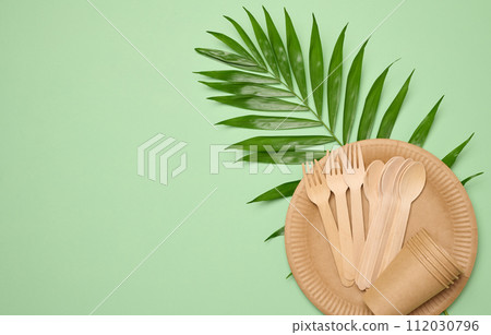 Paper plates and cups, wooden spoons and forks on a green background Paper plates and cups, wooden spoons and forks on a green background 112030796