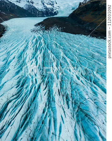 Aerial view of glacier ice cap on wintry region, massive blocks of cracked ice with crevasses in iceland. Spectacular blue diamond shaped rocks creates nordic landscapes, covered frost icebergs. Aerial view of glacier ice cap on wintry region, massive blocks of cracked ice with crevasses in iceland. Spectacular blue diamond shaped rocks creates nordic landscapes, covered frost icebergs. 112031092