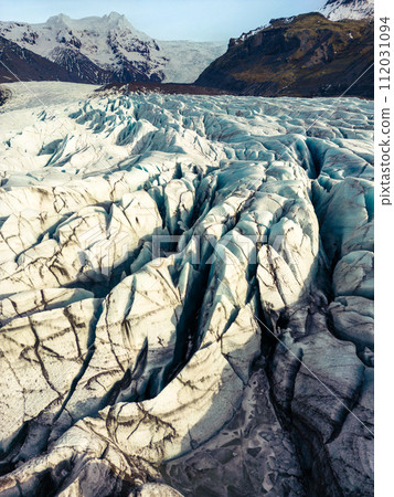 Fantastic vatnajokull glacier in iceland surrounded by freezing cold water and rocky icy hills, icelandic nordic scenery. Massive blue transparent icebergs with frosty rocks and cracks. Fantastic vatnajokull glacier in iceland surrounded by freezing cold water and rocky icy hills, icelandic nordic scenery. Massive blue transparent icebergs with frosty rocks and cracks. 112031094