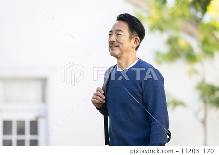 A smiling man in his mid-50s with a backpack on his shoulder 112031170