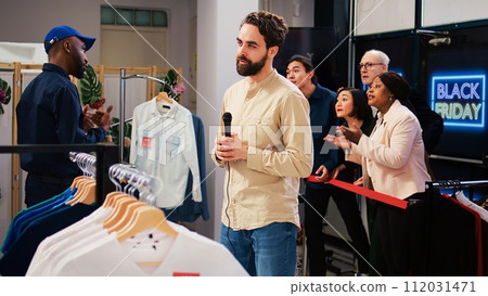 Man reporter recording crazy shoppers at clothing store entrance, broadcasting live black friday news on scene. Male journalist transmitting shopping madness in mall, making media broadcast. 112031471