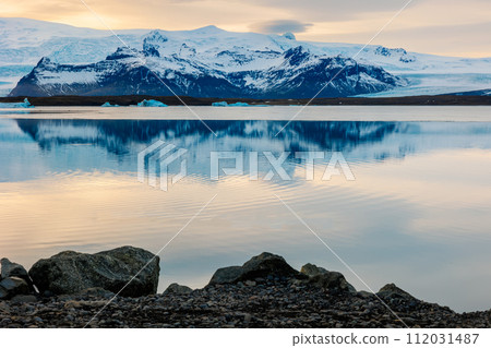 Icy scandinavian big lake in iceland, snowy mountain tops and hills in arctic northern landscape. Beautiful sunset golden hour near frosty natural highland, winter wonderland scenic route. 112031487