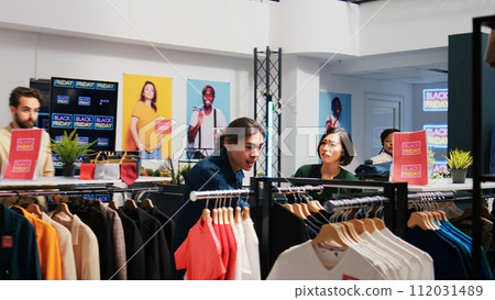 Anxious clients grab discounted clothes, rushing to catch big sales promotions on black friday. Obsessed people taking fashion items at outlet store, shopaholic buyers hunting for bargains. 112031489