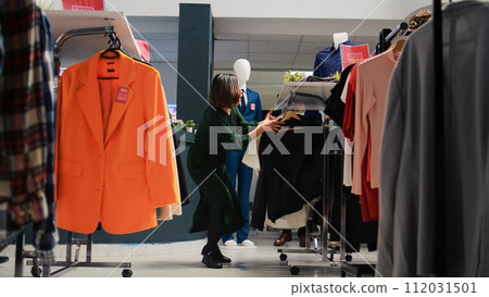 Customer checking fashion items on racks in department store, making purchases at shopping center during black friday promotions. Client buying clothing items from hangers. Handheld shot. Customer checking fashion items on racks in department store, making purchases at shopping center during black friday promotions. Client buying clothing items from hangers. Handheld shot. 112031501