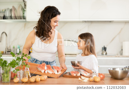 Mom and daughter are preparing festive salmon dish. 112032083