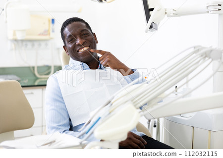 Portrait of positive man pointing at his teeth in dental office Portrait of positive man pointing at his teeth in dental office 112032115